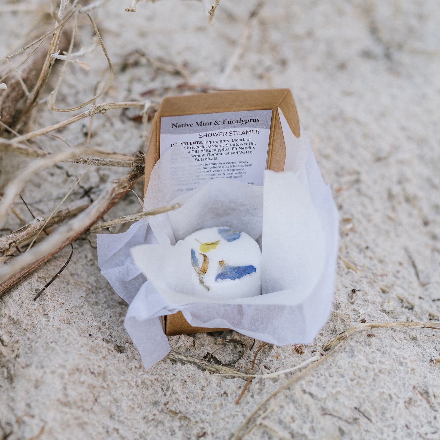 Shower steamer with botanical design in a cardboard box on sandy ground