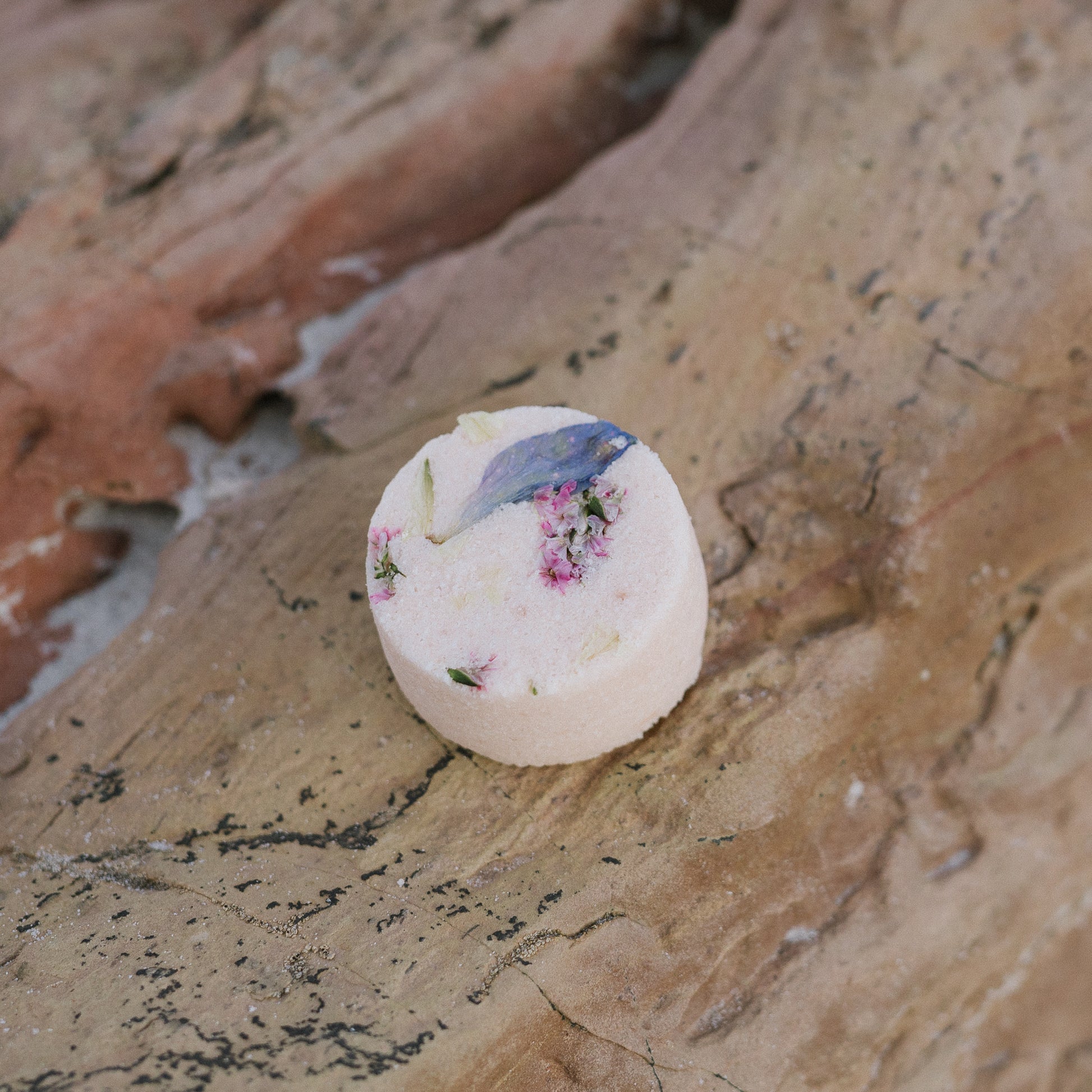 Round mood mist shower steamer on a coastal pink hued rock.