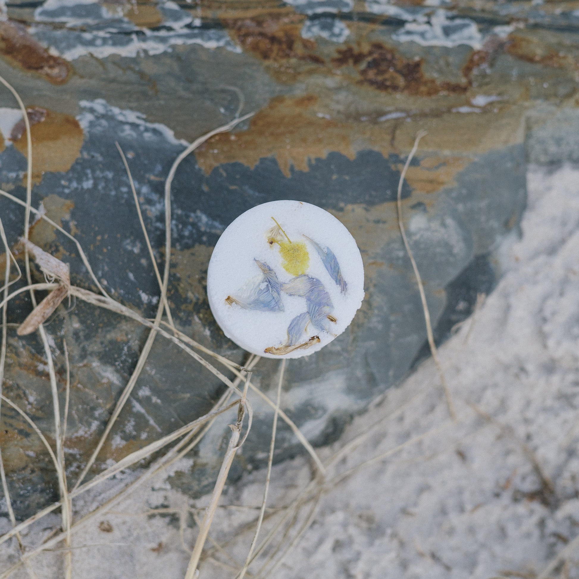 Shower steamer with botasnical pattern sitting on a coastal stone surface.